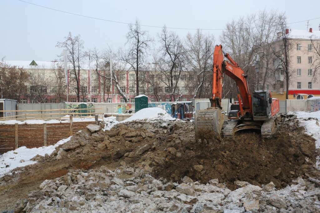 Земляные работы на стройплощадке за временным ограждением в городской застройке